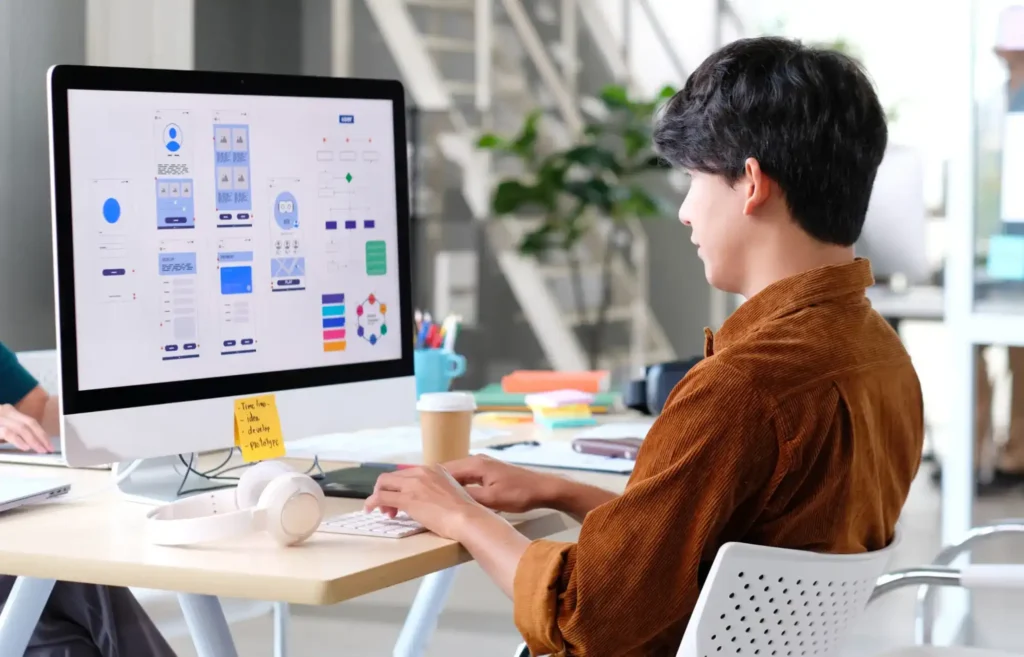 Young man working on UI/UX design wireframes on a computer screen