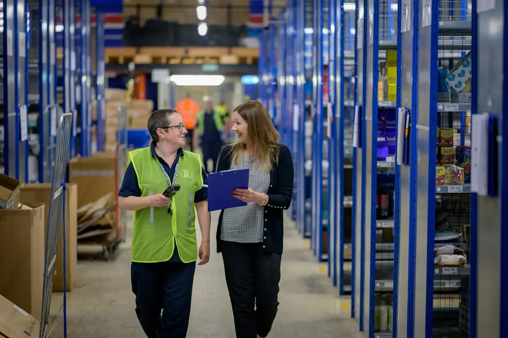 Two women discussing inventory in a warehouse aisle, relevant to hardware industry procurement.